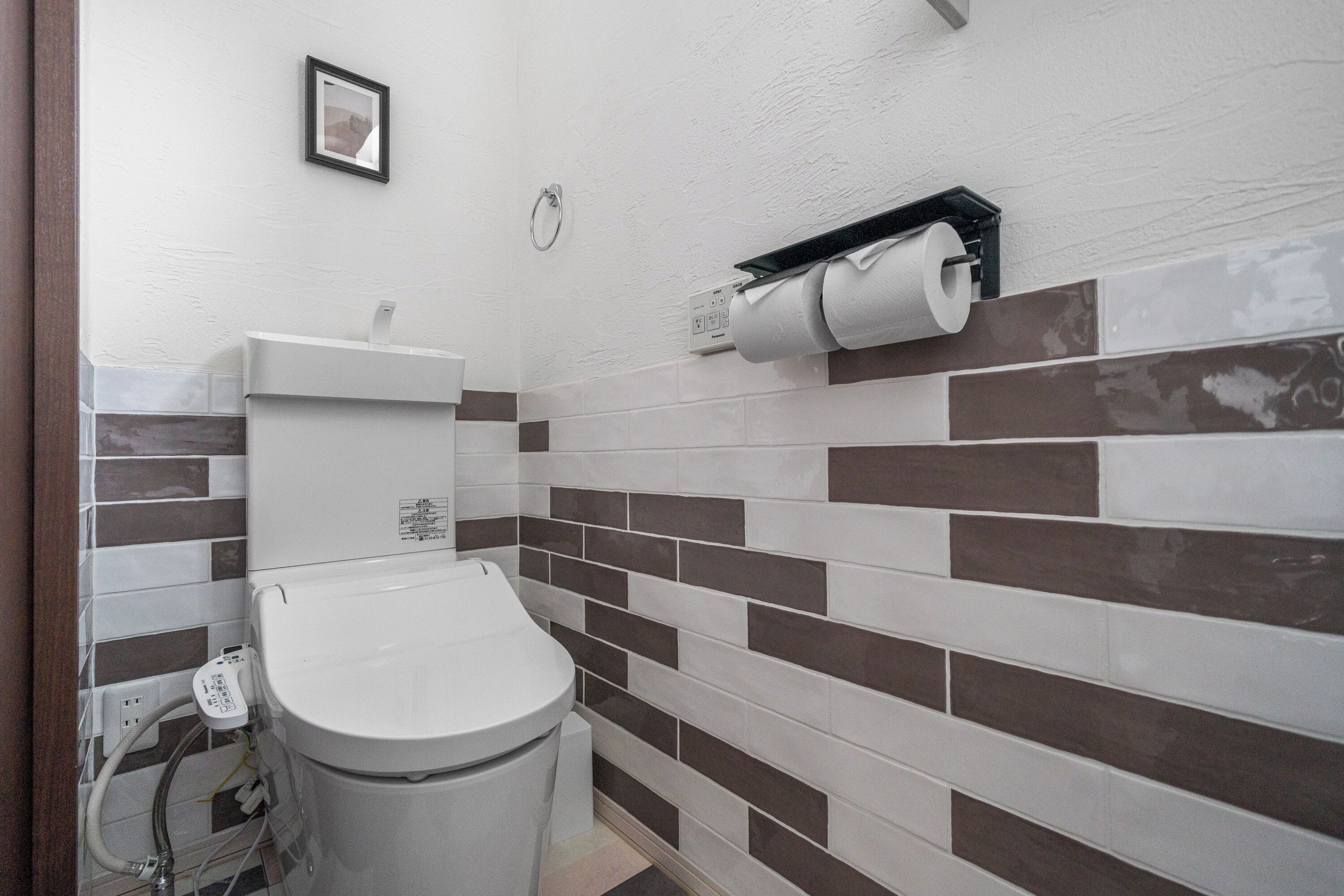 A bathroom with a toilet, a hand dryer, and a towel dispenser.
