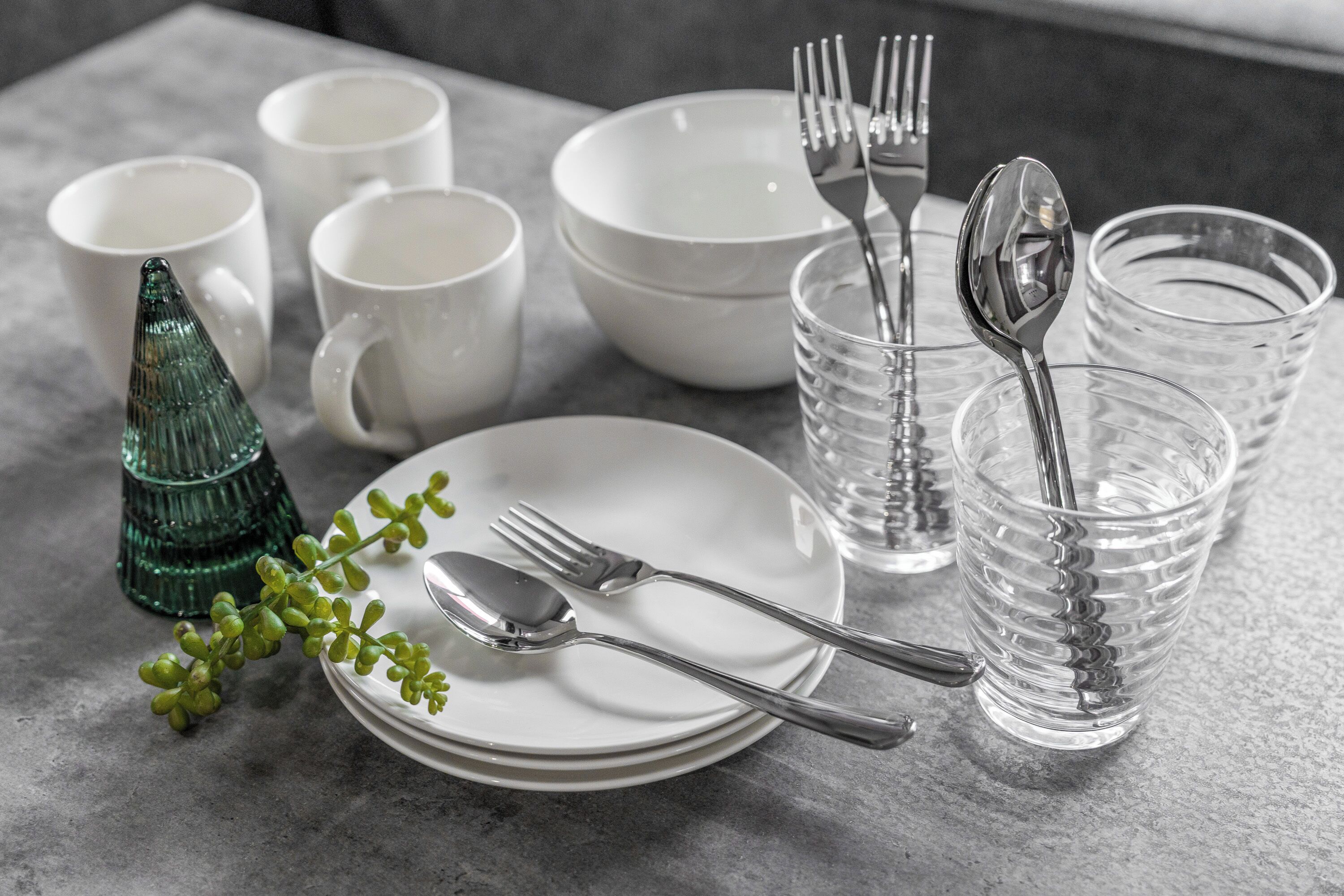A table set with white plates, bowls, cups, and cutlery, along with a green glass ornament.