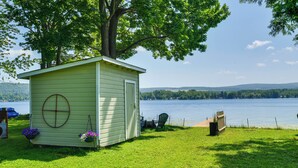 A small shed with a circular window, a table with chairs, and a bench by a lake. - Private Dock & Fire Pit: Beautiful Lake Setting (Bradford)