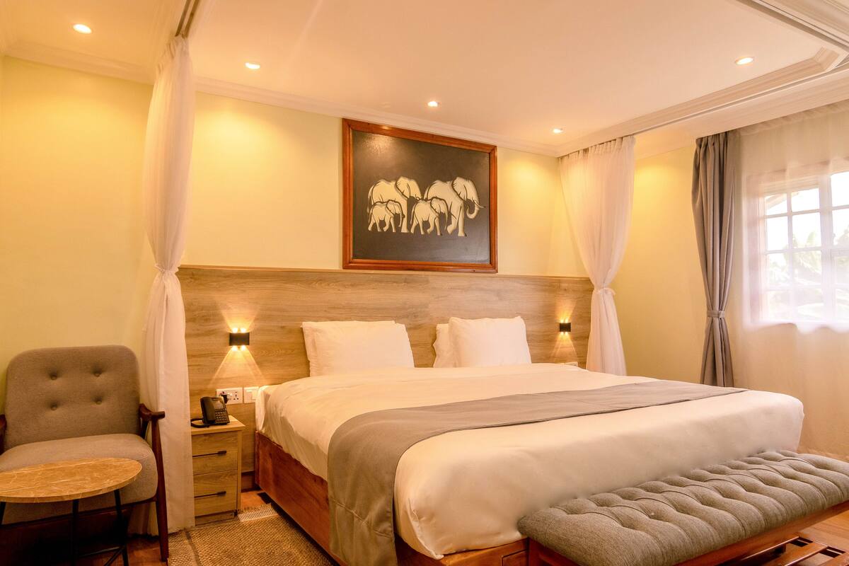Habitación de hotel con una cama grande, mesitas de noche, una silla y un cuadro en la pared.