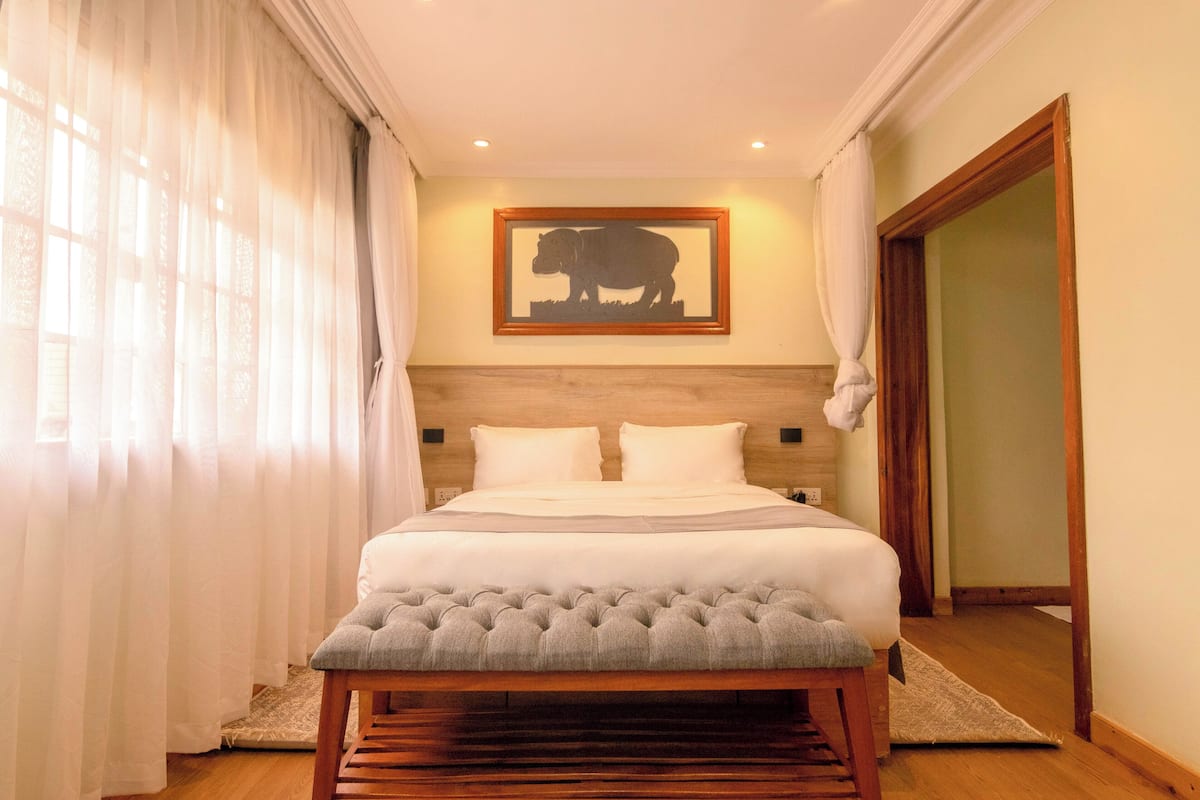 Una cama bien hecha con cabecera capitonada, una silueta de animal enmarcada en la pared y un banco de madera al pie de la cama.