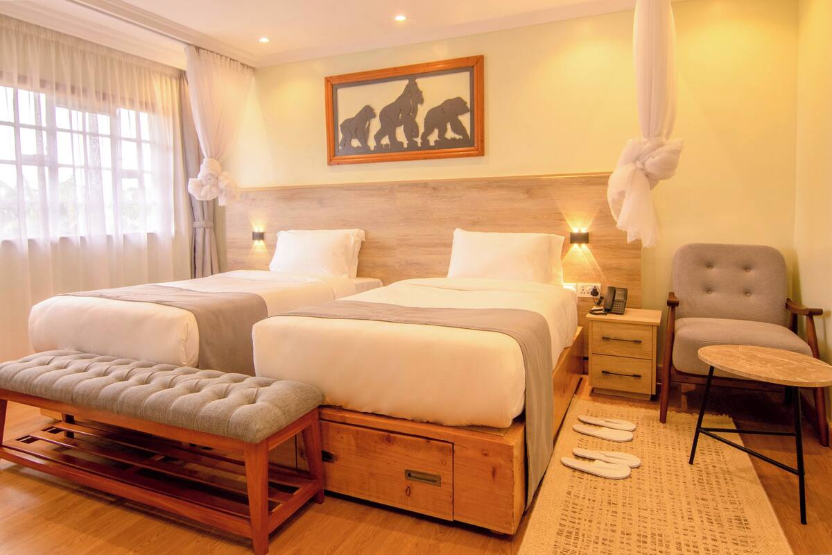 Habitación de hotel con dos camas, un banco, una silla y pantuflas en el suelo.