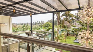 Een glazen balkon met uitzicht op een weelderige tuin, buitenmeubilair en een decoratieve lamp.