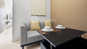A modern dining area with a grey sofa, two yellow cushions, a dark table, and white plates and bowls. - Ocehala by Kozystay - PIK (Jakarta)