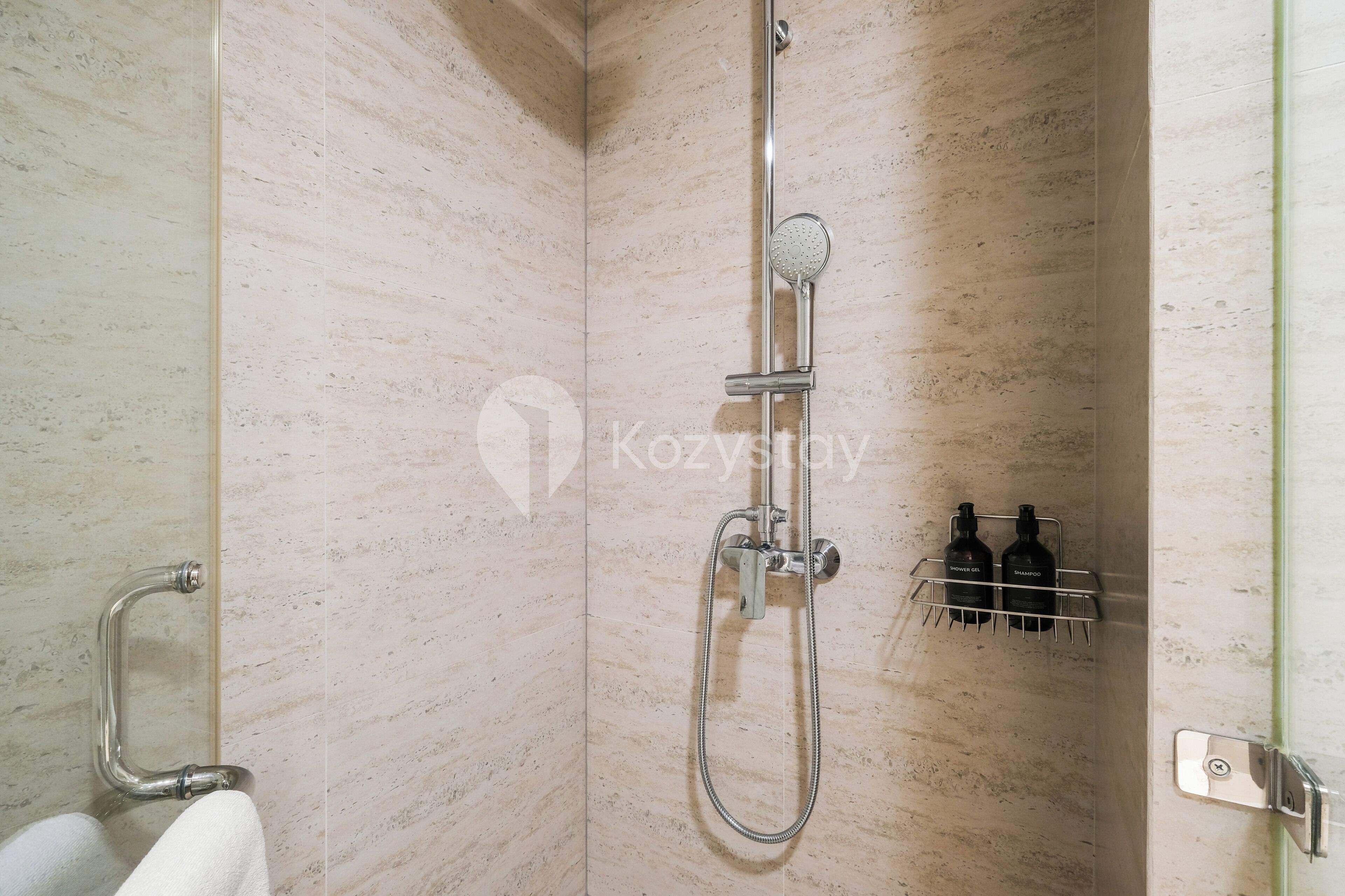 Eine Dusche mit Handbrause, Wandarmatur und Handtuchhalter mit Flaschen.