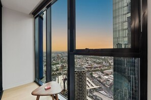 Ein Hotelzimmer in einem Hochhaus mit großem Fenster und Blick auf die Stadtlandschaft, einem kleinen Holzschemel und einem Buch auf dem Fensterbrett.