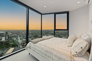 Ein Schlafzimmer mit einem großen Bett, Blick auf eine Stadtlandschaft durch raumhohe Fenster und modernem Design.