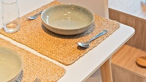Uma sala de jantar moderna com uma mesa posta para dois, uma tigela, um copo e uma colher sobre um descanso de palha.