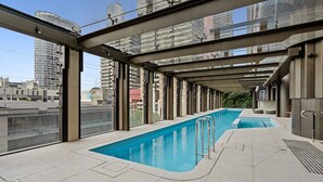 Piscina no terraço com cobertura de vidro, rodeada por edifícios modernos.