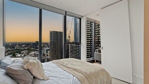 Quarto moderno com uma grande janela com vista para o horizonte urbano ao pôr do sol.