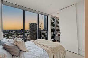 Ein modernes Schlafzimmer mit großem Fenster und Blick auf eine Stadtlandschaft bei Sonnenuntergang.