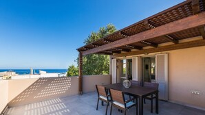 A covered patio with a table and chairs, overlooking a coastal view. - Philoxenia Residences (Mylopotamos)