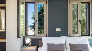A bedroom with a bed, two bedside tables, a night lamp, and a window with a view of trees. - Philoxenia Residences (Mylopotamos)