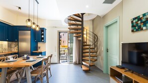 A modern kitchen with blue cabinets, a wooden dining table, and a spiral staircase leading to another level. - Philoxenia Residences (Mylopotamos)