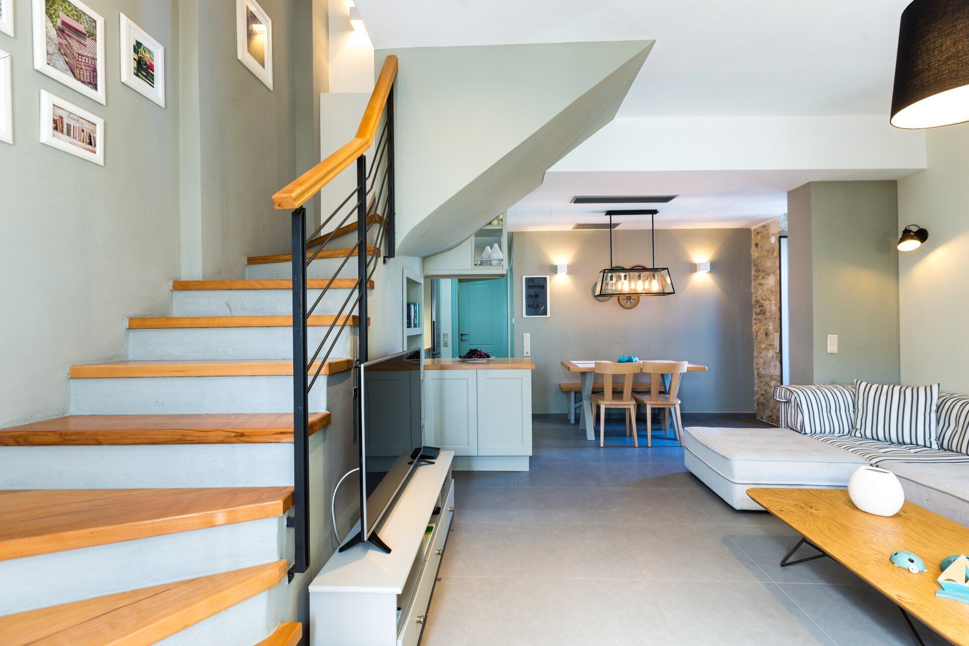 A modern interior with a wooden staircase, a kitchen area, a dining space, and a seating area with a sofa and striped cushions.