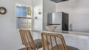 A kitchen with a stainless steel refrigerator, a bowl on the counter, and two wicker chairs.
