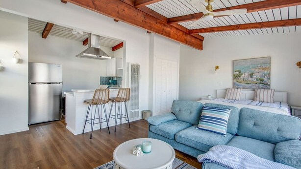 A modern living room with a sofa, a dining area with chairs, a kitchen with a fridge, and a ceiling fan.