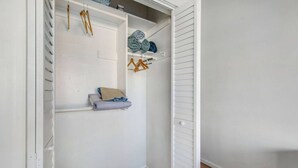 A white closet with shelves, hanging space, and a wooden hanger rack.