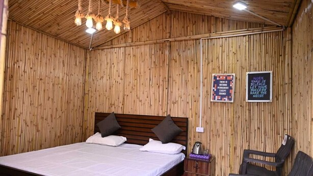 A room with a wooden wall and ceiling, a bed with white bedding, two pillows, a nightstand with a lamp, and two chairs. - Sanskriti Homestay & Cottage (Dhari)