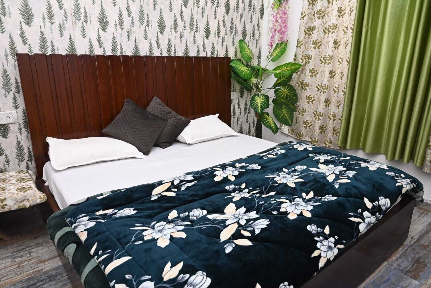 A neatly made bed with a dark floral duvet, a wooden headboard, and a green plant beside it.
