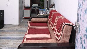 A living room with a sofa, a coffee table, and a television. There is a door leading to another room and a wall-mounted light fixture. - Sanskriti Homestay & Cottage (Dhari)