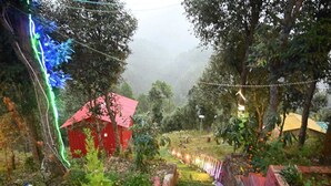 A red-roofed building surrounded by greenery and trees, with a misty background. - Sanskriti Homestay & Cottage (Dhari)