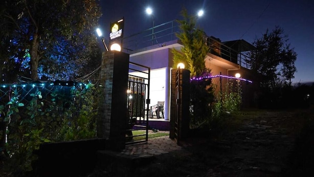 A modern building with a glass entrance, surrounded by trees and illuminated by string lights. - Sanskriti Homestay & Cottage (Dhari)
