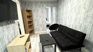 A room with a black sofa, a wooden side table, a small black table, and a wooden shelving unit. - Awesome 2 Bedroom in downtown (London)