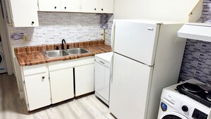 A compact kitchen with white cabinets, a wooden countertop, a built-in sink, a white refrigerator, and a front-loading washing machine. - Awesome 2 Bedroom in downtown (London)