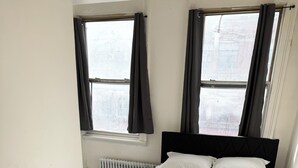 A bedroom with a bed, two windows with curtains, a radiator, and a light-colored wooden floor. - Awesome 2 Bedroom in downtown (London)