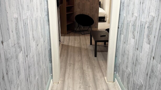 A narrow hallway with wooden flooring and walls, leading to a room with a bed and a chair. - Awesome 2 Bedroom in downtown (London)