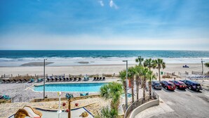 Un hotel frente a la playa con piscina, sillas de playa y aparcamiento.