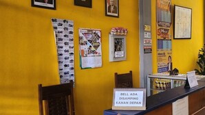 A reception area with a yellow wall, framed portraits, a calendar, and a sign indicating a disinfection station. - OYO 94933 Wisma Cha Tatami Palangkaraya (Palangkaraya)