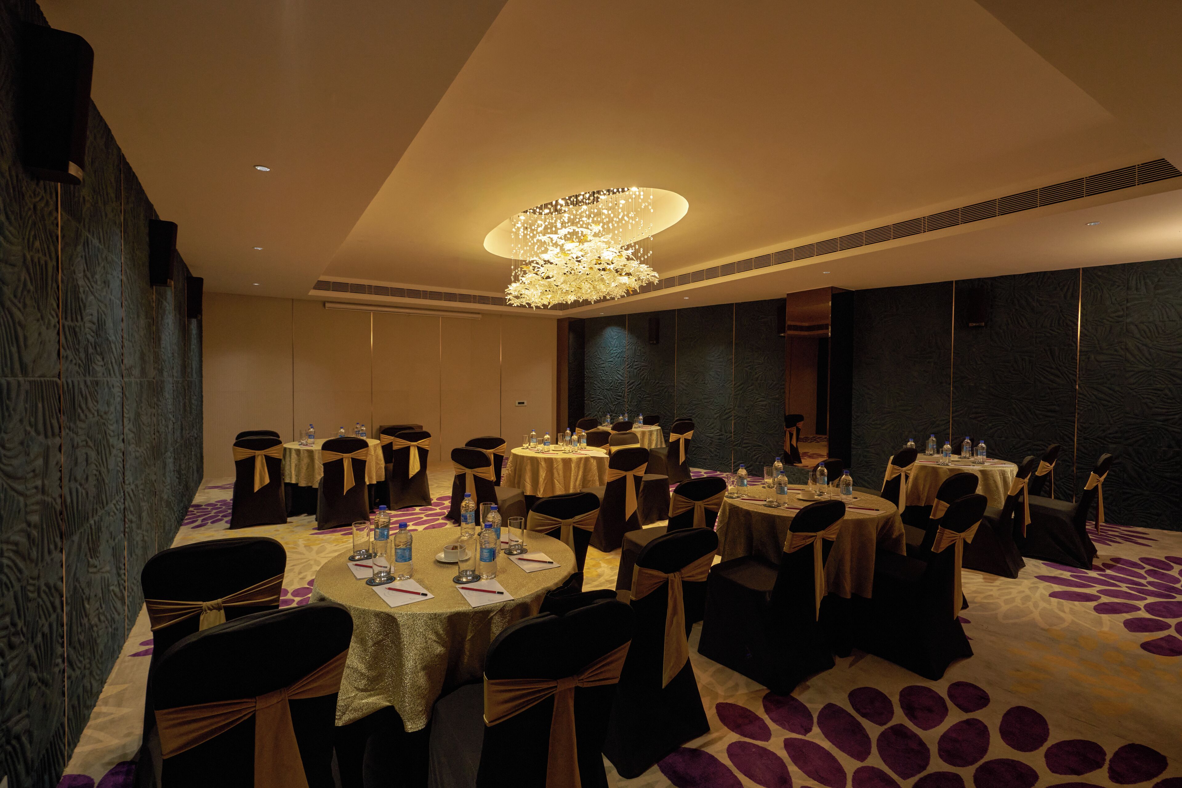 A banquet hall with round tables, chairs, and a central chandelier.