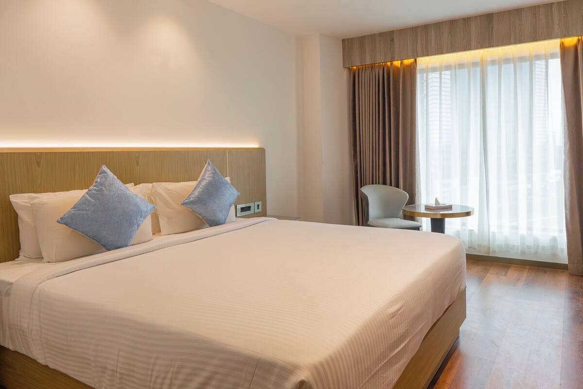 A hotel room with a large bed, two pillows, a bedside table, a chair, and a window with curtains.