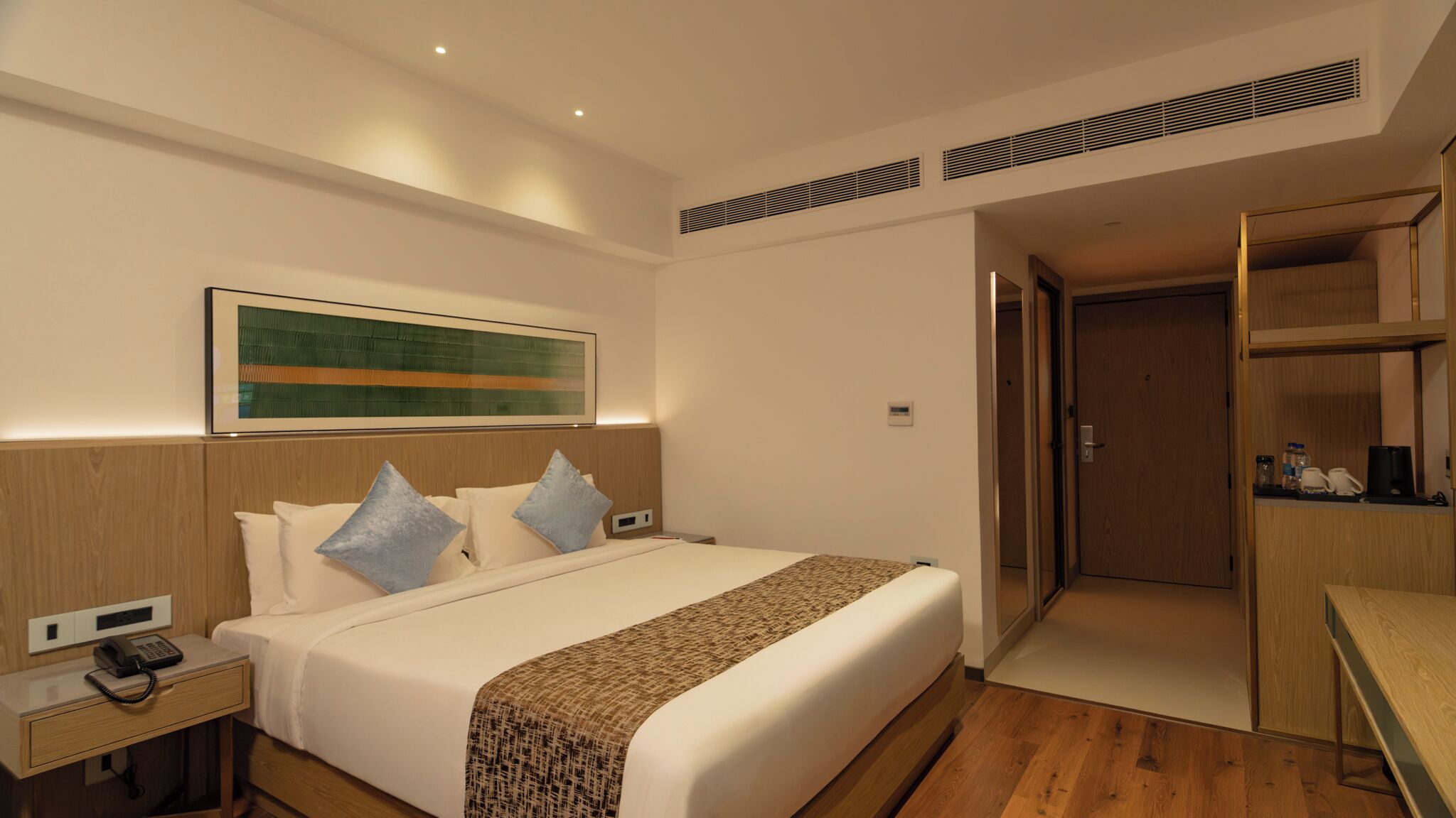 A modern hotel room with a large bed, bedside table, and a desk area.