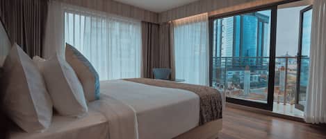 A modern hotel room with a large bed, a chair, and a view of a cityscape through large windows.
