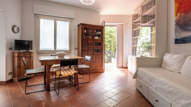 Una sala de estar con un sofá, un televisor, una mesa de comedor con sillas, una estantería y una ventana con cortinas.