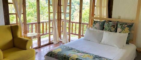 A room with a bed, a yellow armchair, and large windows with curtains.
