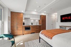 Une chambre d’hôtel moderne équipée d’un lit, d’une télévision, d’une kitchenette et d’une salle de bain.