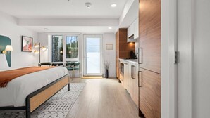 Ein modernes Hotelzimmer mit Bett, Schreibtisch, Küchenzeile und Blick ins Freie.