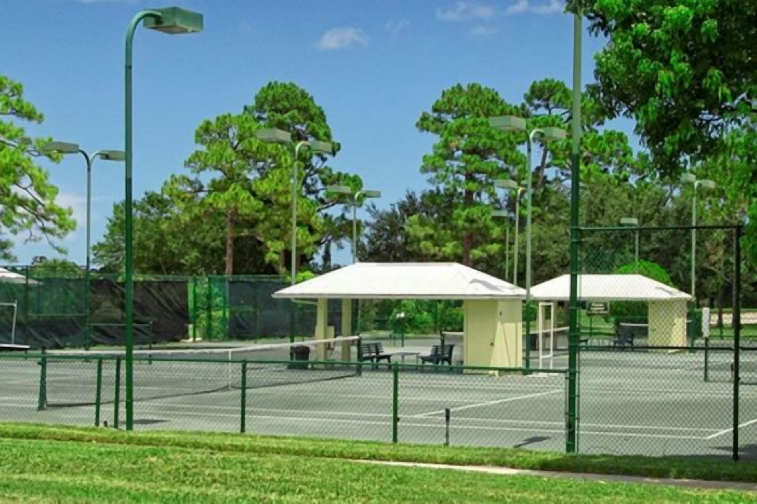 A tennis court with a fence, benches, and a covered seating area.
