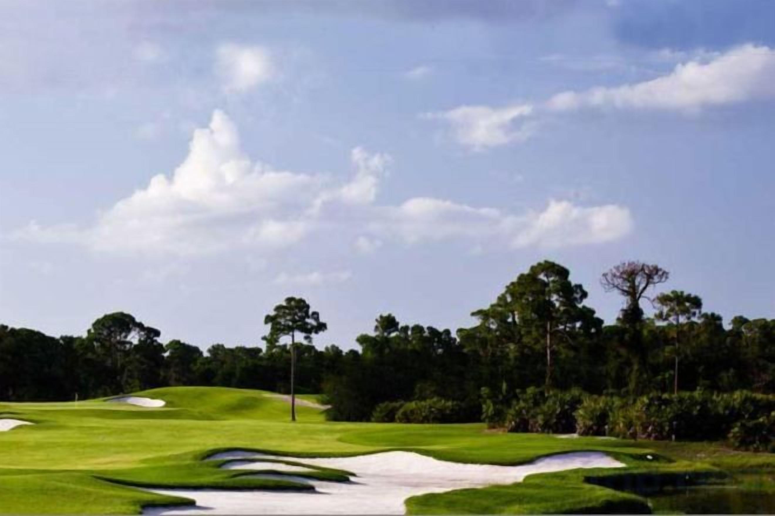 Campo de golfe com bunkers de areia, árvores e céu limpo.