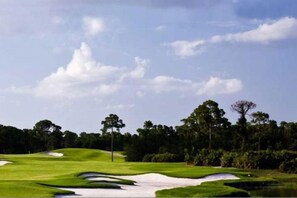 Ein Golfplatz mit Sandbunkern, Bäumen und blauem Himmel.