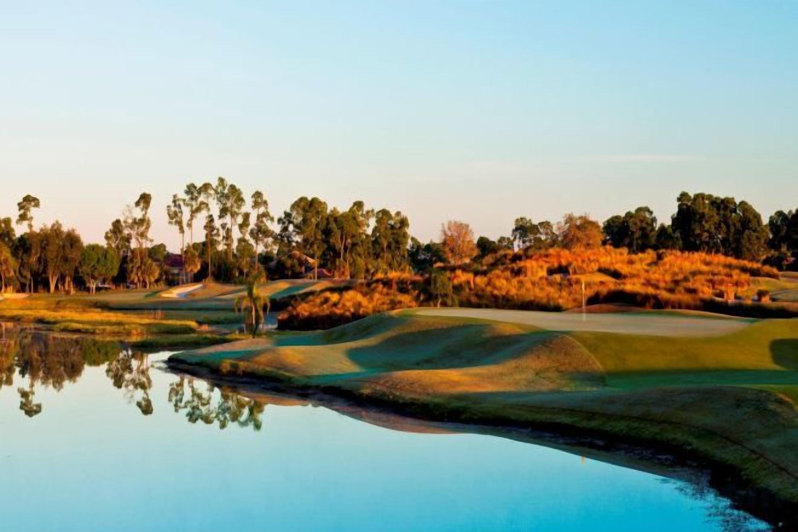 A golf course with a water body reflecting the landscape, surrounded by trees and grassy areas.
