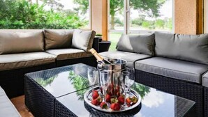 A modern outdoor seating area with a glass-top table, a metal drink tray with glasses and strawberries, and a sofa with cushions. - PgaVillageResort by AmericanVacationLiving 2 Br (St. Lucie County)