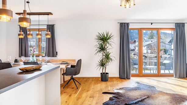 A modern kitchen with a central island, a dining area with a chair, and a large window with curtains. - Apartment 'Luisa' with Mountain View, Private Terrace and Wi-Fi (Scharnitz)