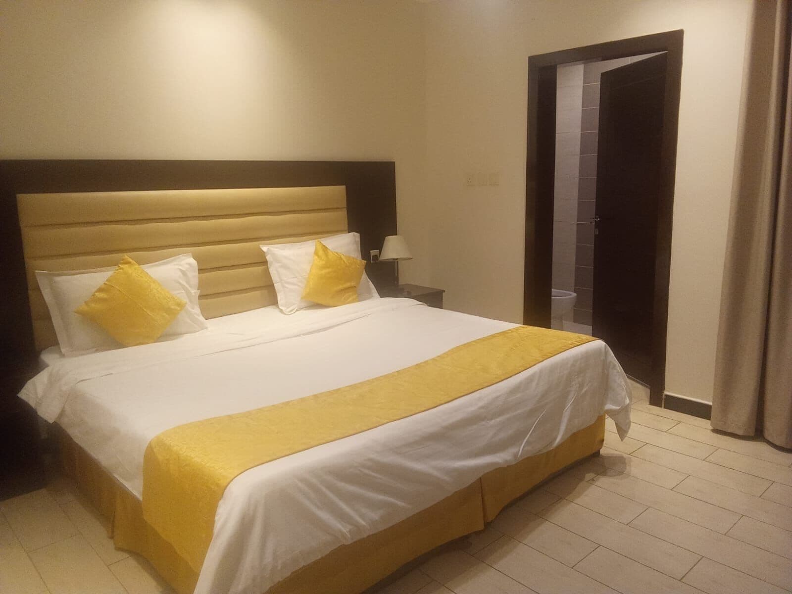 Una habitación de hotel con una cama grande, una mesita de noche y la puerta del baño.