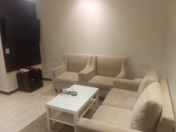 Una sala de estar con una mesa de centro blanca, sofás color beige, un televisor en la pared y un mueble negro pequeño.