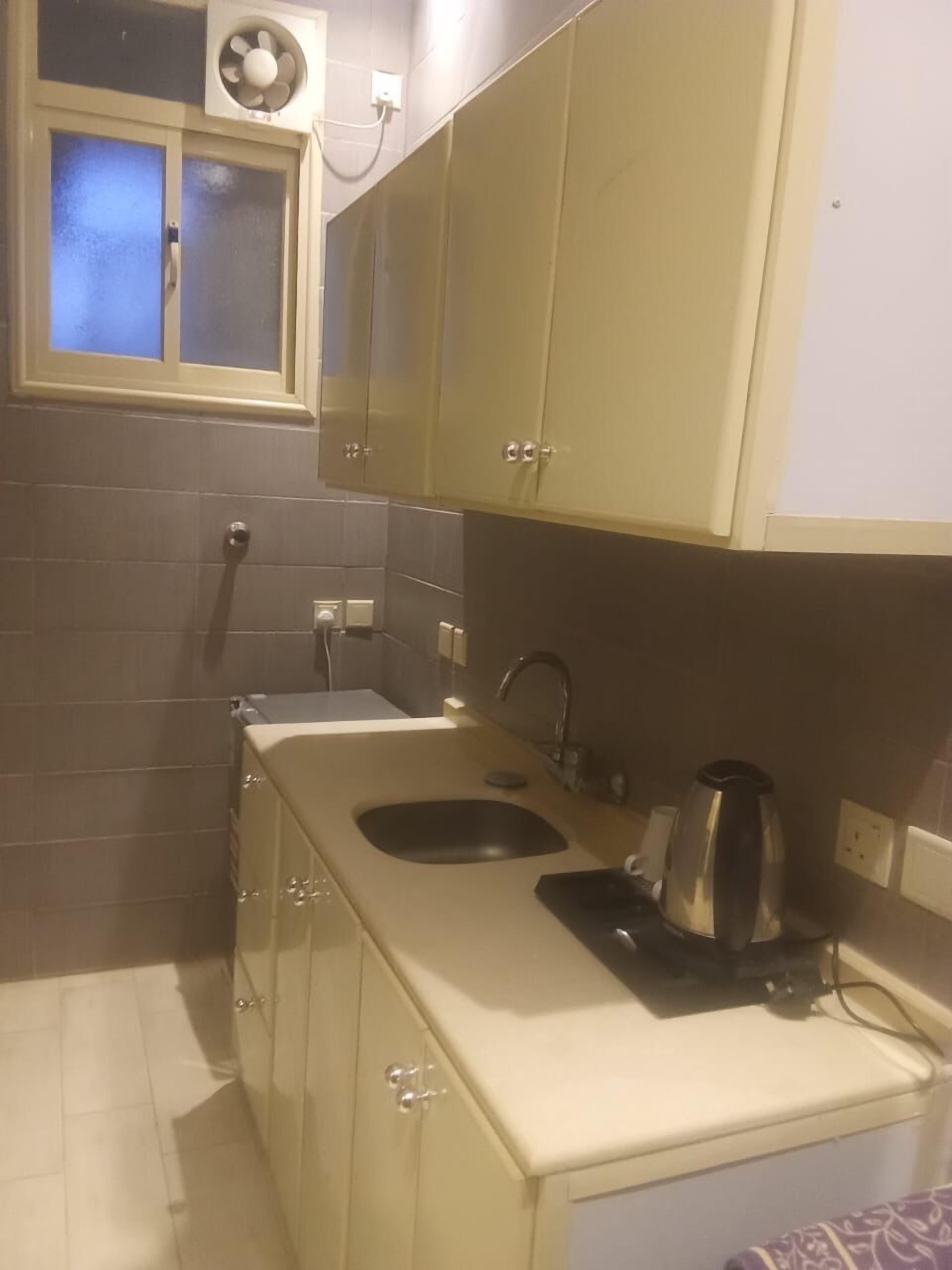 A compact kitchen with a sink, a kettle, and cabinets.